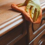 Close-up of craftsman applying wood stain with cloth to antique table showing proper technique and rich color penetrating wood grain