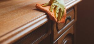 Close-up of craftsman applying wood stain with cloth to antique table showing proper technique and rich color penetrating wood grain